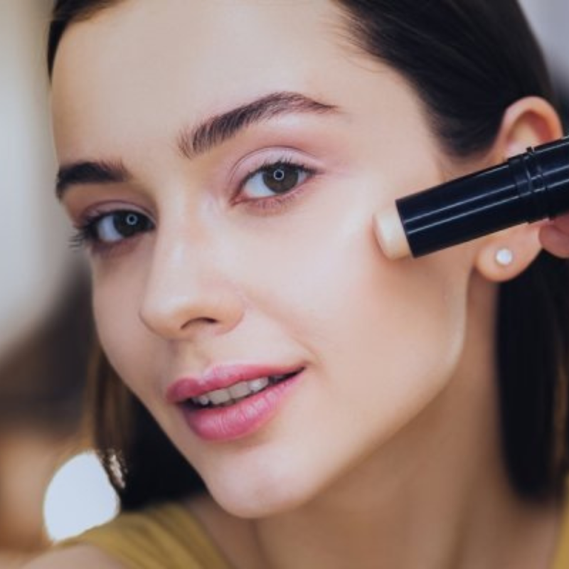 Femme appliquant un correcteur sur sa joue