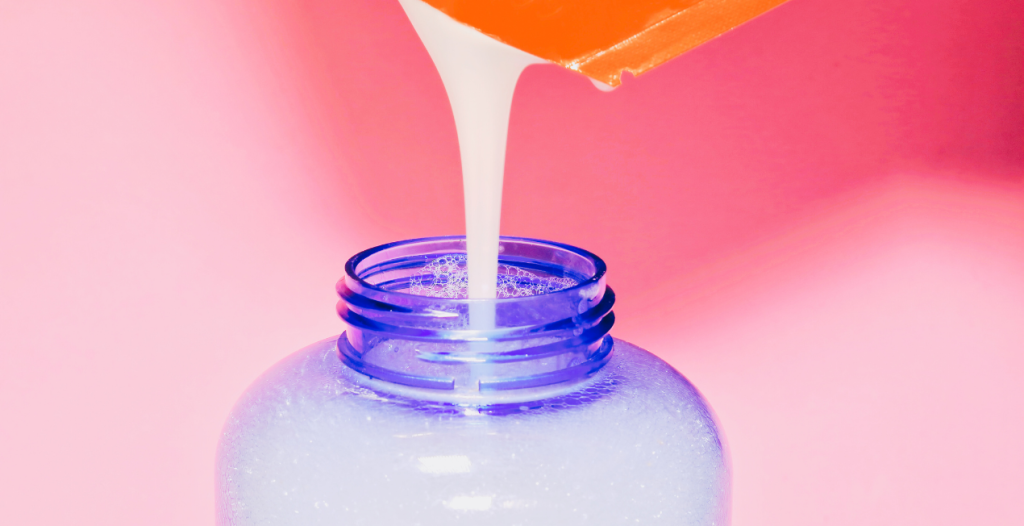 Lait versé dans un flacon bleu, fond rose.