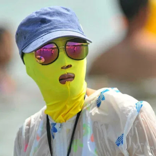 Personne masquée sur la plage, chapeau et lunettes.