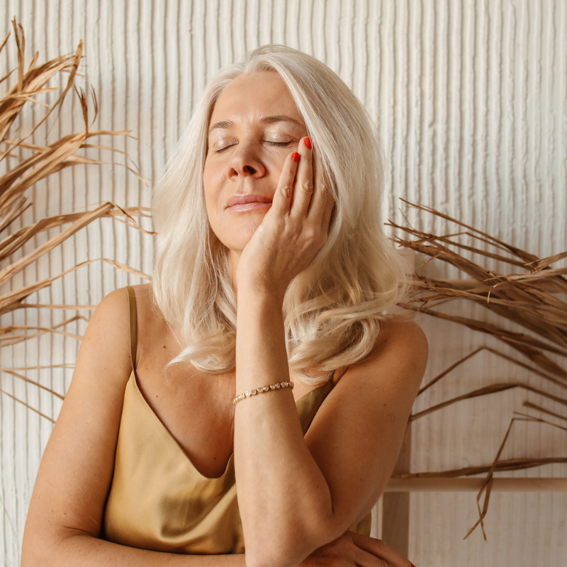 Femme détendue, cheveux blonds, main sur visage.