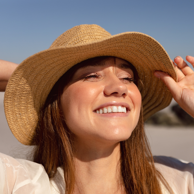 Femme souriante portant un chapeau de paille au soleil.