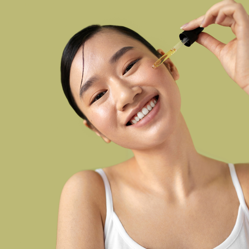 Femme appliquant du sérum visage, fond vert.