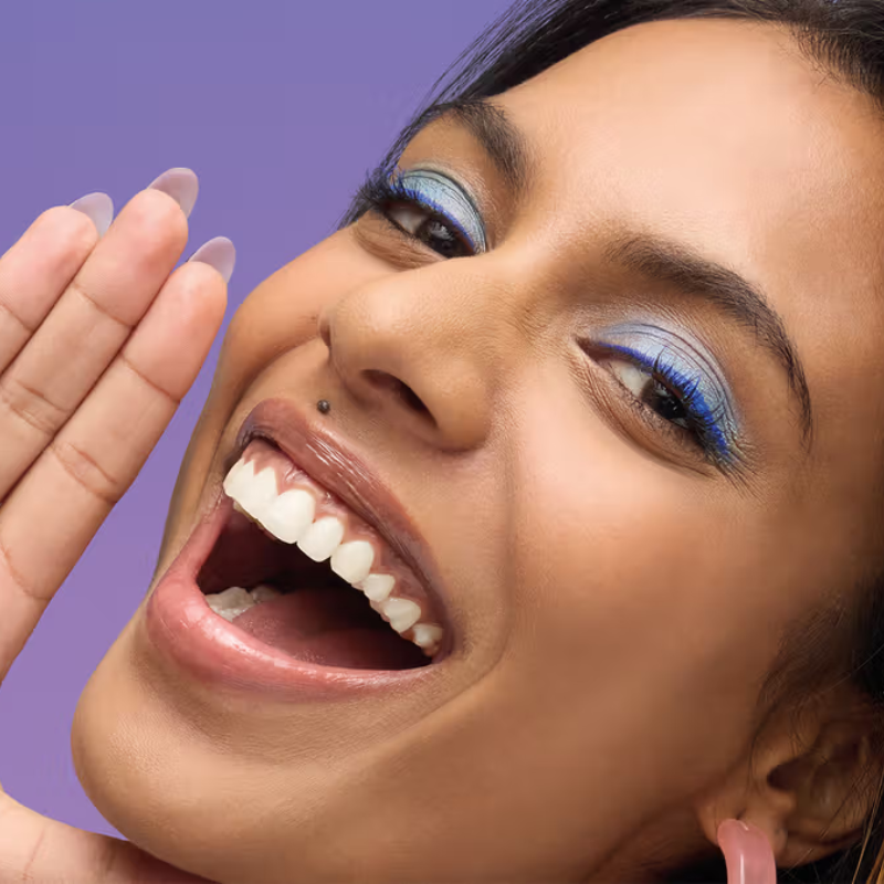 Femme souriante maquillage bleu, dent visible.