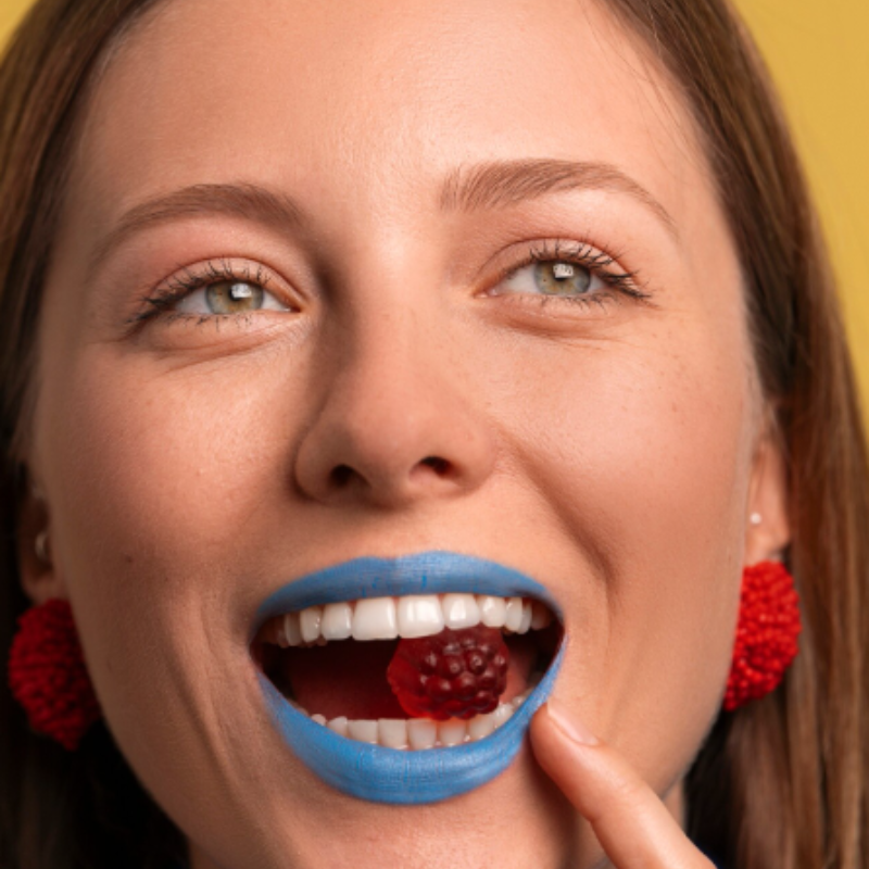 Femme mangeant une framboise avec du rouge à lèvres bleu.
