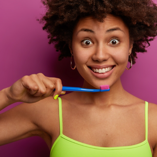 Femme souriante brosse ses dents, fond rose vif.