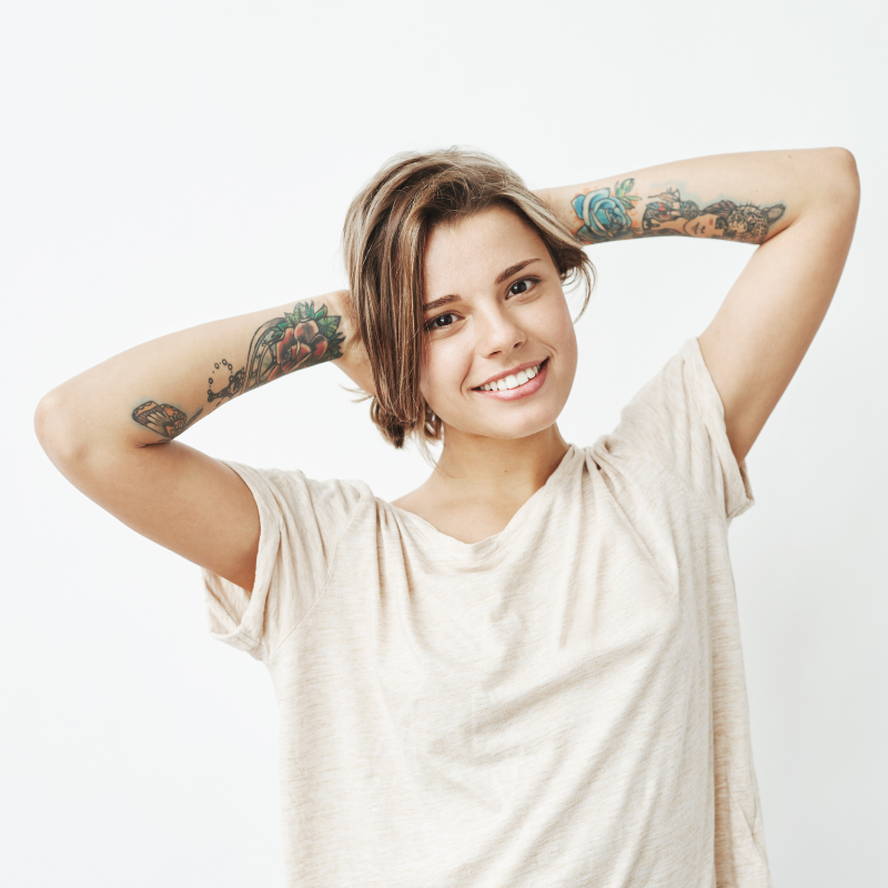 Femme souriante avec tatouages, bras levés.