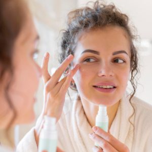 Femme appliquant crème visage devant miroir.